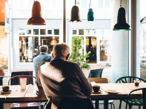 Older man sitting in a cafe drinking coffee.