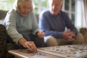 A woman and man sitting on a couch putting together a jigsaw puzzle.